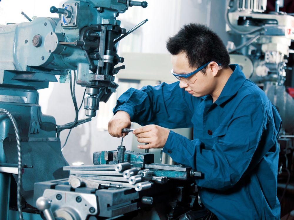 Trabalhador operando máquina de usinagem em ambiente industrial durante processo de fabricação de peças metálicas.